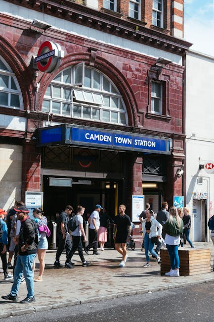 The entrance of Camden Town underground station, featuring a red brick facade with arched windows and an underground sign. Above the entrance, a blue sign displays the station name 'Camden Town Statio